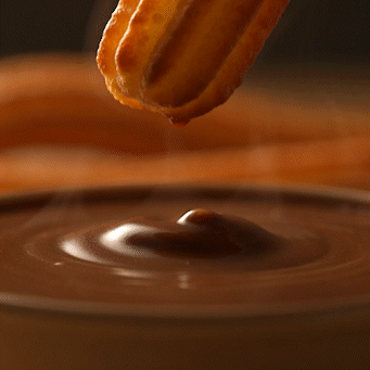Churro sumergido en chocolate caliente, textura brillante y fondo desenfocado.